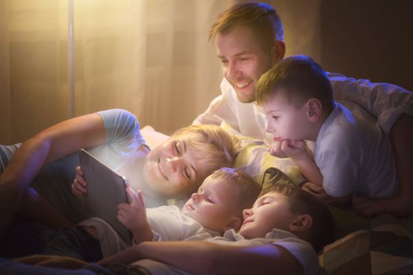 خانواده شاد - پدر مادر و سه بچه که شب ها روی مبل دراز کشیده اند و از رایانه لوحی استفاده می کنند خانواده بزرگ با هم در حال تماشای فیلم روی رایانه لوحی در اتاق تاریک با هم بودن