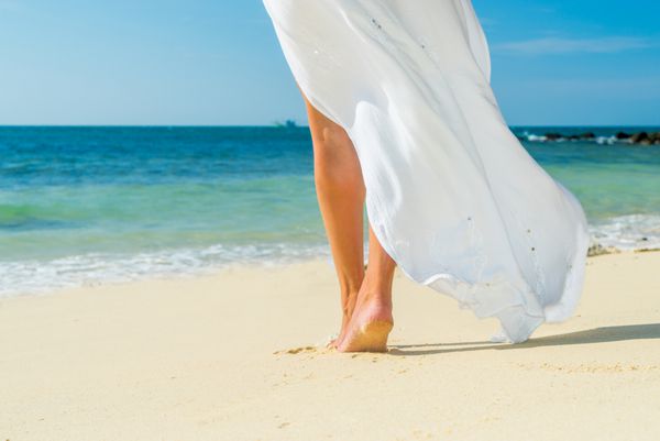 زن جوان با لباس سفید در حال قدم زدن در ساحل