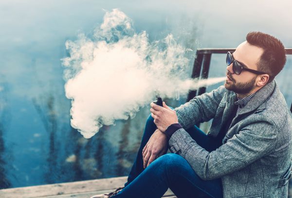 مردی با ریش که سیگار الکترونیکی در فضای باز بخار می دهد