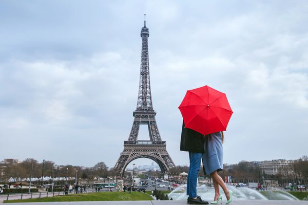 ماه عسل در پاریس زوج در حال بوسیدن پشت چتر قرمز مقابل برج ایفل
