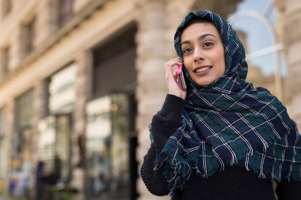 زن جوان با حجاب در شهر در حال صحبت با تلفن همراه