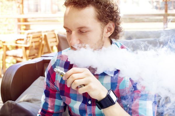 مرد خوش تیپ مدرن در حال کشیدن سیگار الکترونیکی در کافه در فضای باز