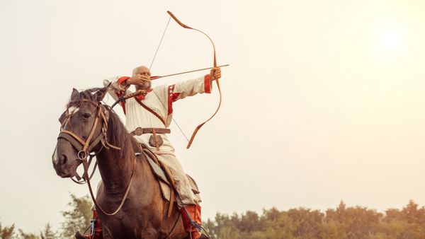مردی با لباس قومی سوار بر اسب است و از کمان نشانه می گیرد