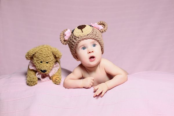 کودک ترسناک بامزه با کلاه بافتنی و خرس عروسکی در زمینه صورتی