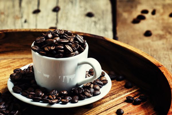 دانه های قهوه برشته شده در یک فنجان سفید پس زمینه چوبی قدیمی