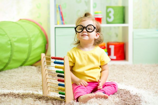 دختر بچه عینکی می زد که با اسباب بازی چرتکه در داخل خانه بازی می کرد