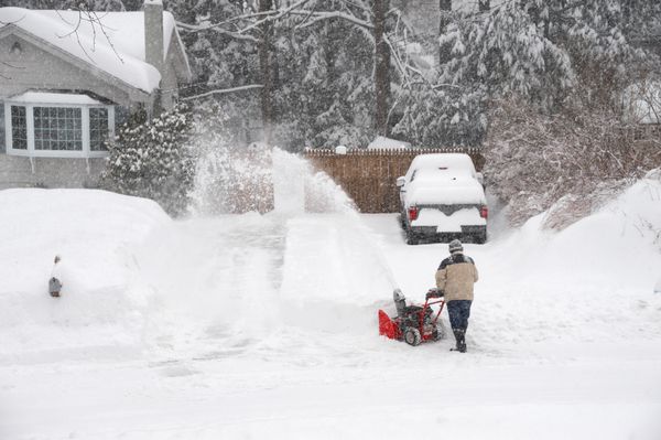 مردی که در حال برف‌کشی در مسیر خانه توسط برف‌دم است
