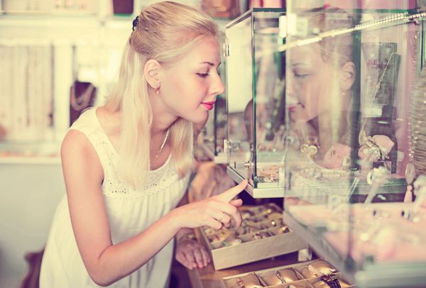 زن خندان در حال انتخاب جواهر فروشی در ویترین شیشه ای