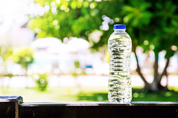بطری پلاستیکی با آب ایستاده در تابستان درختان و استخر در پس زمینه