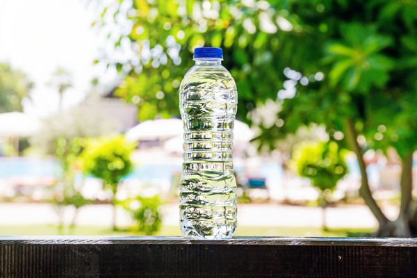 بطری پلاستیکی آب که روی تابستان درختان و استخر در پس‌زمینه ایستاده است