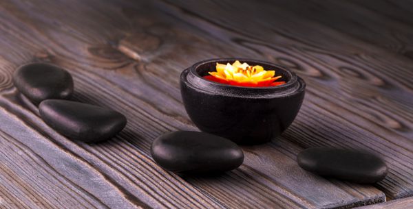 سنگ های سیاه و یک شمع در زمینه چوبی