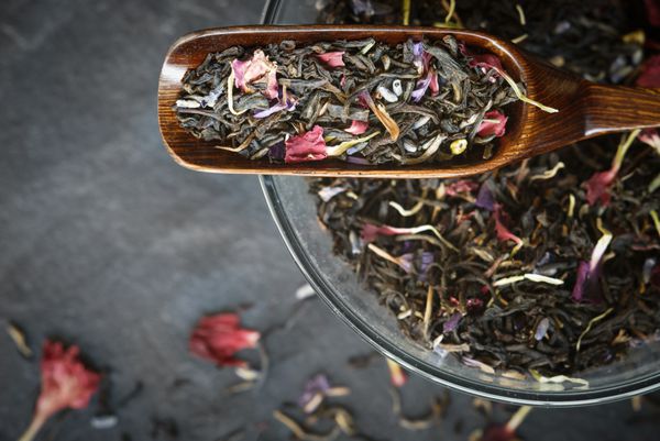 چای سیاه با گلبرگ های گل در نمای بالای قاشق چوبی