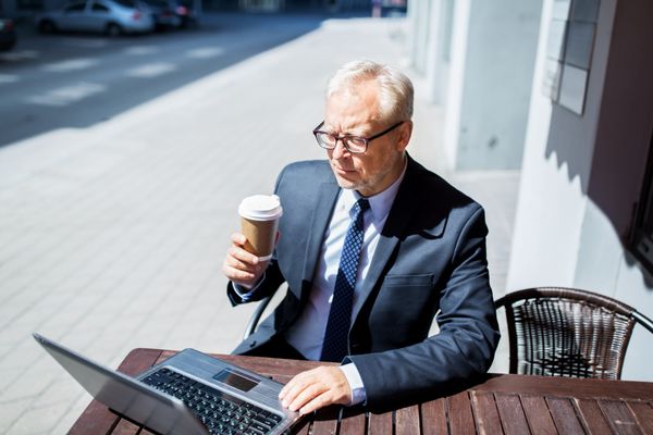 تاجر ارشد با لپ تاپ در حال نوشیدن قهوه