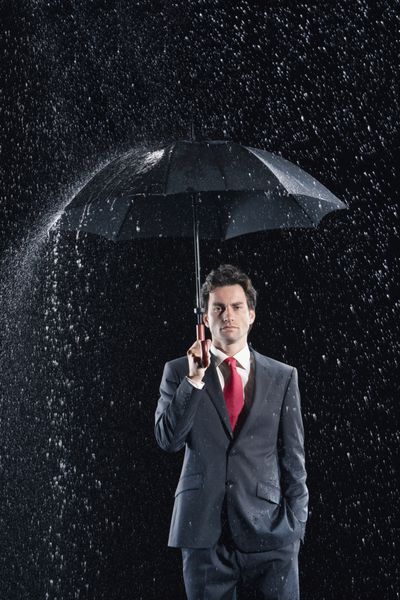 پرتره یک تاجر جوان که زیر چتر زیر باران در برابر پس زمینه سیاه ایستاده است