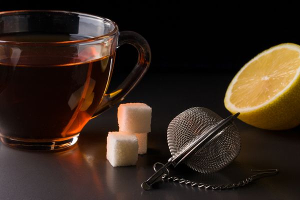 فنجان چای با یک صافی و لیمو در زمینه تیره