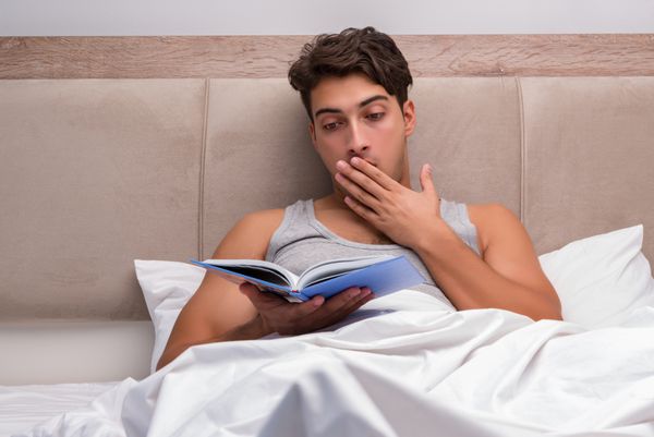 مردی که روی تخت در حال خواندن کتاب است