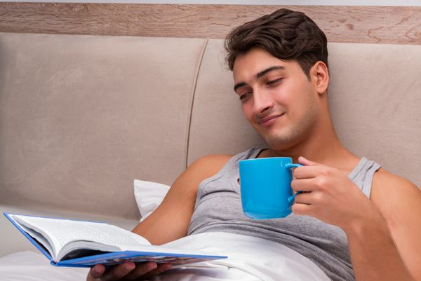 مردی که روی تخت در حال خواندن کتاب است
