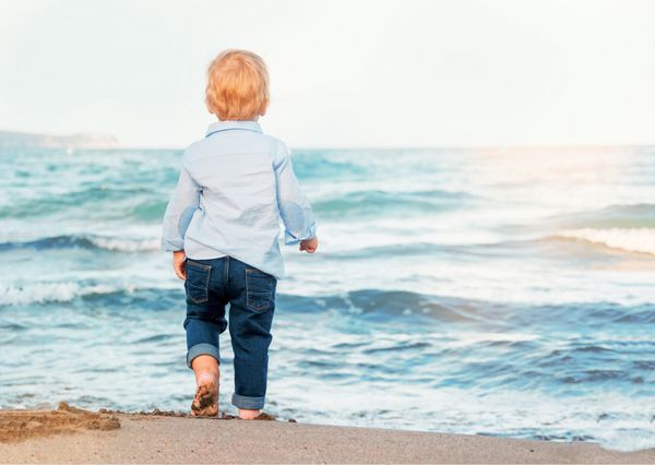 پسر بچه ناز در ساحل دریا را تحسین می کند پاهای برهنه خوشحال