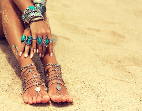 پا و دست زن در ساحل گرمسیری با شن و ماسه اعضای بدن پای دختر برنزه با جواهرات نقره دستبند و انگشتر با فیروزه