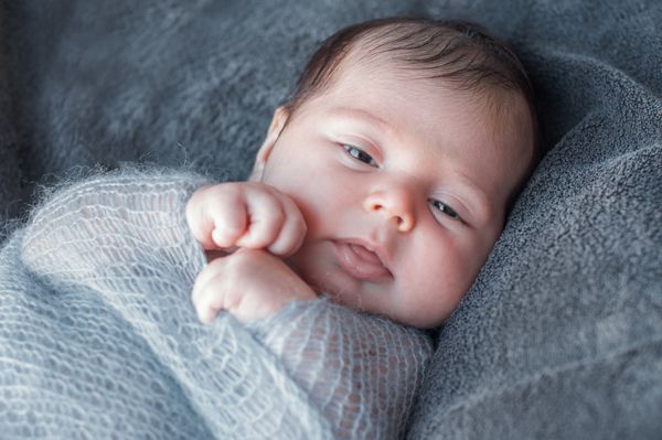 نوزاد تازه متولد شده در پتوی گرم بافتنی پیچیده شده است پرتره نزدیک زیبا از یک نوزاد تازه متولد شده که بیدار است و به اطراف نگاه می کند بچه دسته پتوها را کشید