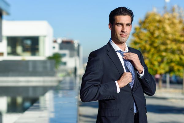 تاجر جوان خوش تیپ در حال تنظیم کراوات در پس زمینه شهری