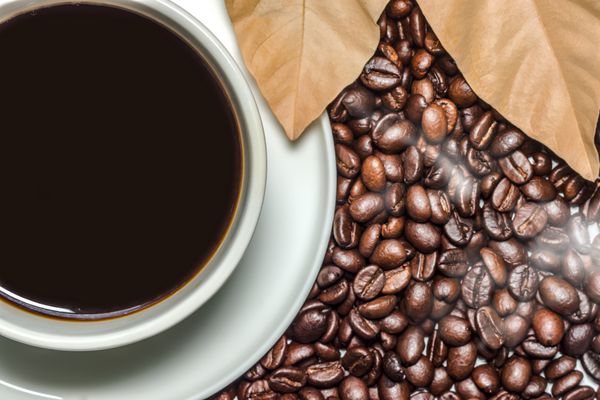 قهوه سیاه در فنجان و پس‌زمینه دانه‌های قهوه برشته شده را تار می‌کند