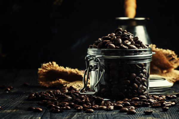 دانه های قهوه عربیکا برشته شده در یک شیشه روی پس زمینه سیاه فوکوس انتخابی