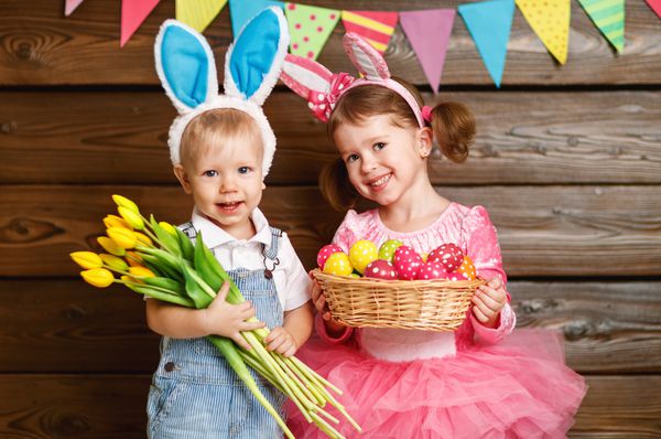 دختر و پسر بچه های شاد با لباس خرگوش عید پاک با سبد تخم مرغ و گل