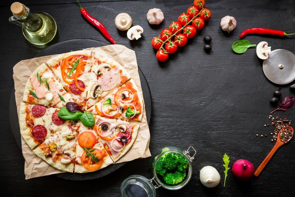 قاب غذا - پیتزا ایتالیایی با مواد تشکیل دهنده و ادویه جات ترشی جات در پس زمینه تیره تخت خوابیده نمای بالا