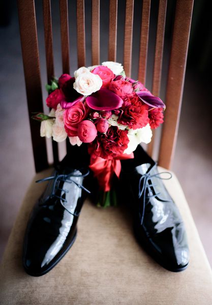 دسته گل عروسی ساخته شده از گل های قرمز روی کفش های لاکی ایستاده است