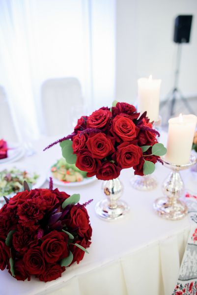 دسته گل های کوچک رز قرمز روی میز شام سفید قرار دارند