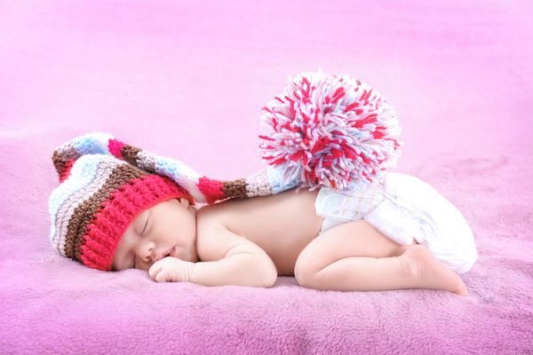 نوزاد کوچولوی ناز با کلاه حصیری که روی تخت در خانه می خوابد