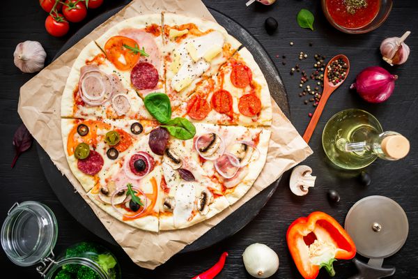 پیتزا ایتالیایی با مواد و سبزیجات ادویه جات ترشی جات در پس زمینه تیره تخت خوابیده نمای بالا