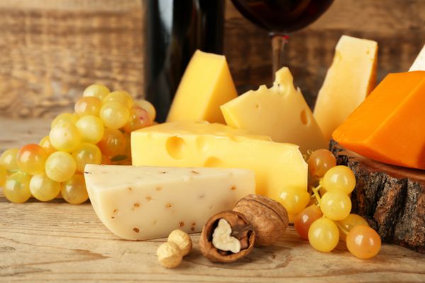 شراب قرمز و کنده با انواع پنیر در زمینه چوبی