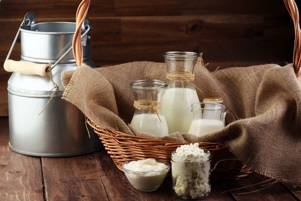 محصولات لبنی - لبنیات سالم و خوشمزه روی میز خامه ترش در یک کاسه سفید کاسه پنیر خامه در بانک و شیشه شیر بطری شیشه ای و در یک لیوان