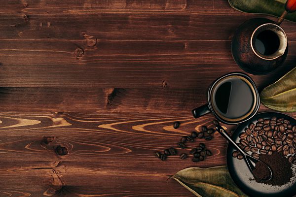 قهوه داغ در فنجان سیاه با دانه‌ها برگ‌های خشک و گلدان ترکی با فضای کپی روی پس‌زمینه تخته چوبی قدیمی قهوه‌ای نمای بالا سبک روستیک