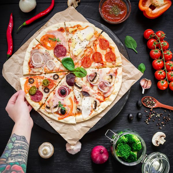 پیتزای خوشمزه ایتالیایی با مواد ادویه و دست زن روی میز تاریک تخت خوابیده نمای بالا