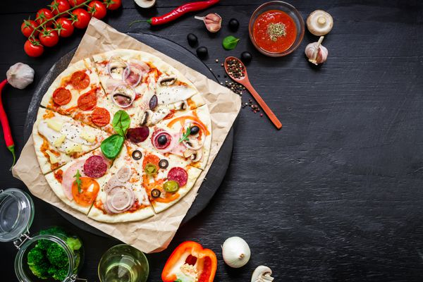 قاب غذا پیتزای ایتالیایی با مواد و ادویه ها در پس زمینه تیره تخت خوابیده نمای بالا