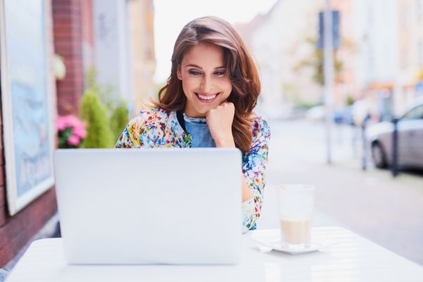 زن شاد در حال خواندن اخبار روی لپ تاپ خود در کافه خارج از منزل