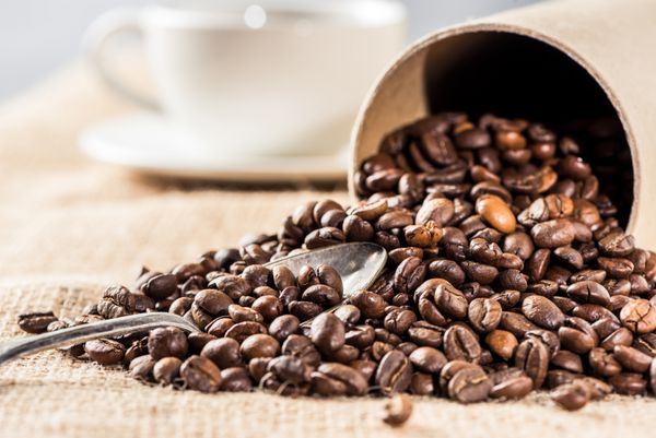 دانه های قهوه معطر با قاشق پراکنده از جعبه مقوایی