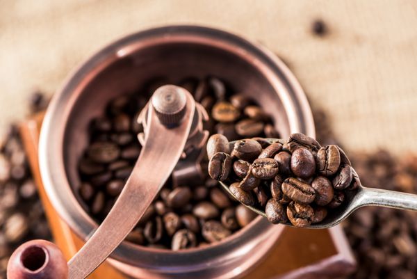 نمای مرتفع آسیاب قهوه با دانه های قهوه معطر در قاشق