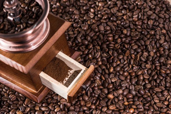 نمای مرتفع آسیاب قهوه با قهوه آسیاب شده روی دانه های قهوه