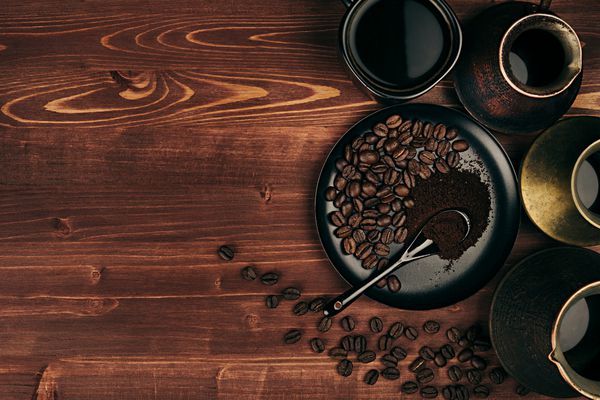 قهوه داغ در فنجان سیاه و قابلمه های ترکی با دانه ها نعلبکی با فضای کپی روی پس زمینه تخته چوبی قدیمی قهوه ای نمای بالا سبک روستیک