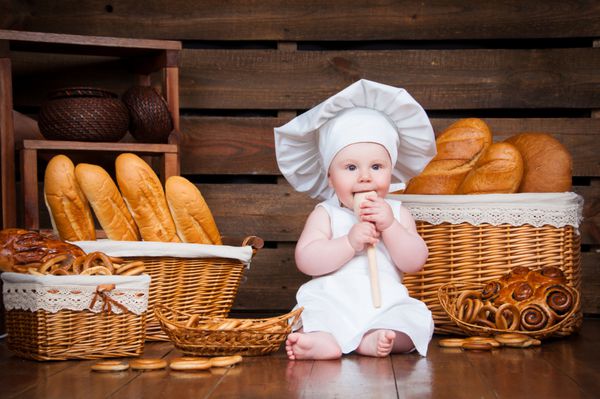 کودک آشپزی در حال خوردن شیرینی روی پس زمینه سبدهایی با رول و نان