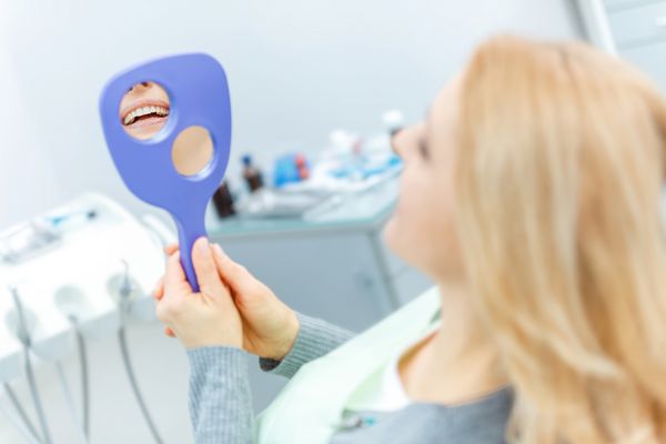 نمای عقب زن بلوند زیبا با آینه در معاینه دندانپزشکی