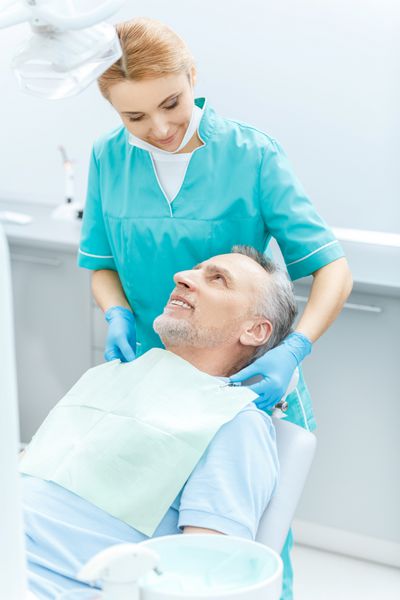 دندانپزشک حرفه ای خندان و بیمار بالغ که در مطب دندانپزشکی به یکدیگر نگاه می کنند
