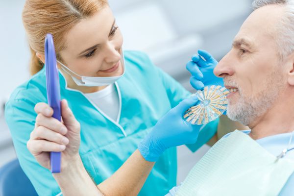 دندانپزشک حرفه ای با نمونه های مقایسه دندان های بیمار بالغ که به آینه نگاه می کند