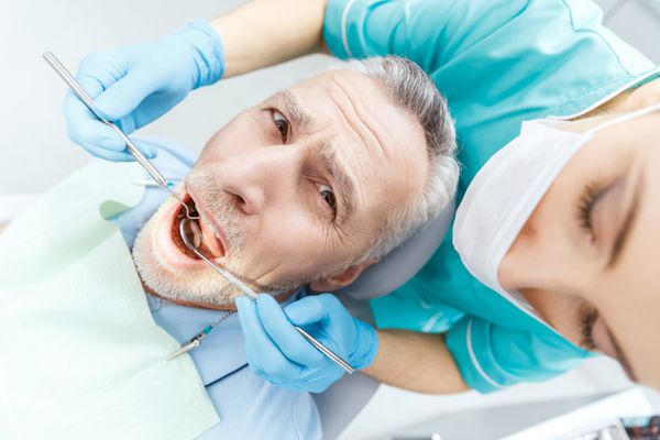 عکس برش خورده دندانپزشک حرفه ای در حال درمان بیمار بالغ ترسیده در کلینیک دندانپزشکی