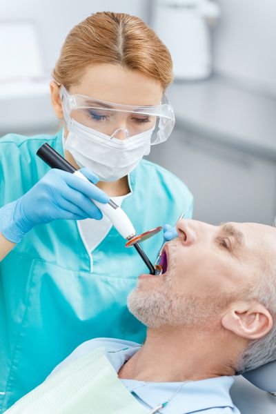 دندانپزشک حرفه ای با استفاده از لامپ UV کیورینگ دندان روی دندان های بیمار بالغ
