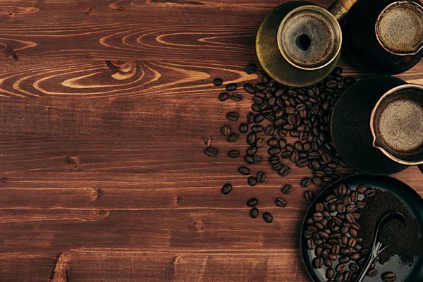 قهوه داغ در ظروف ترکی کهنه با دانه‌ها نعلبکی با فضای کپی روی پس‌زمینه تخته چوبی قدیمی قهوه‌ای نمای بالا سبک روستیک